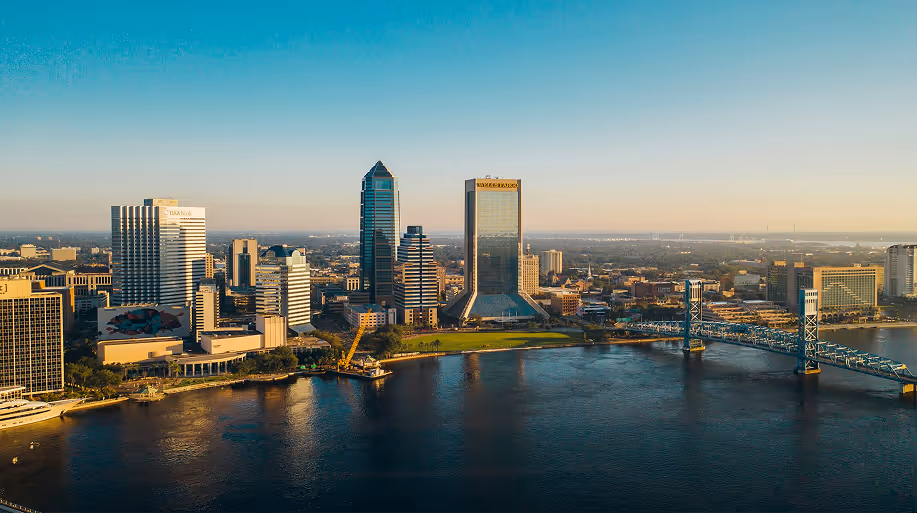 Aerial view of Jacksonville, Florida skyline with the St. Johns River and Main Street Bridge at sunset.