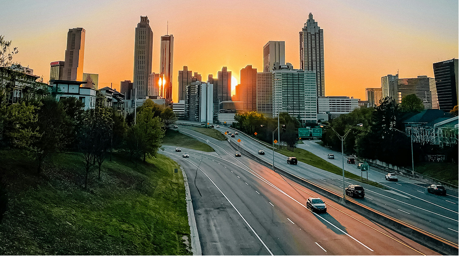 Sunset over a highway leading into a city skyline with tall buildings and scattered cars.