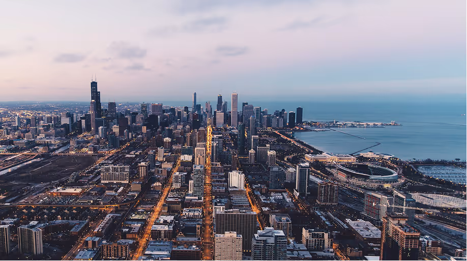 Aerial view of Chicago skyline at dusk with illuminated streets and Lake Michigan in the background.