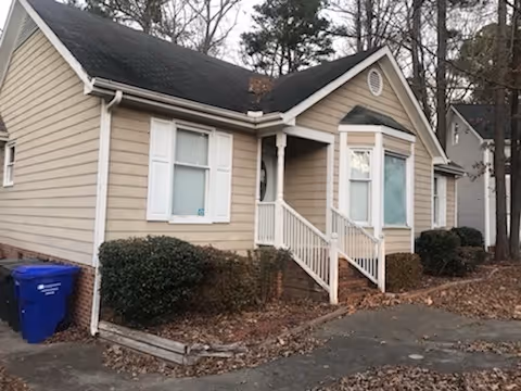 Single-story house with white exterior and black trim, a small front porch with stairs, landscaped front yard with grass and colorful plants.
