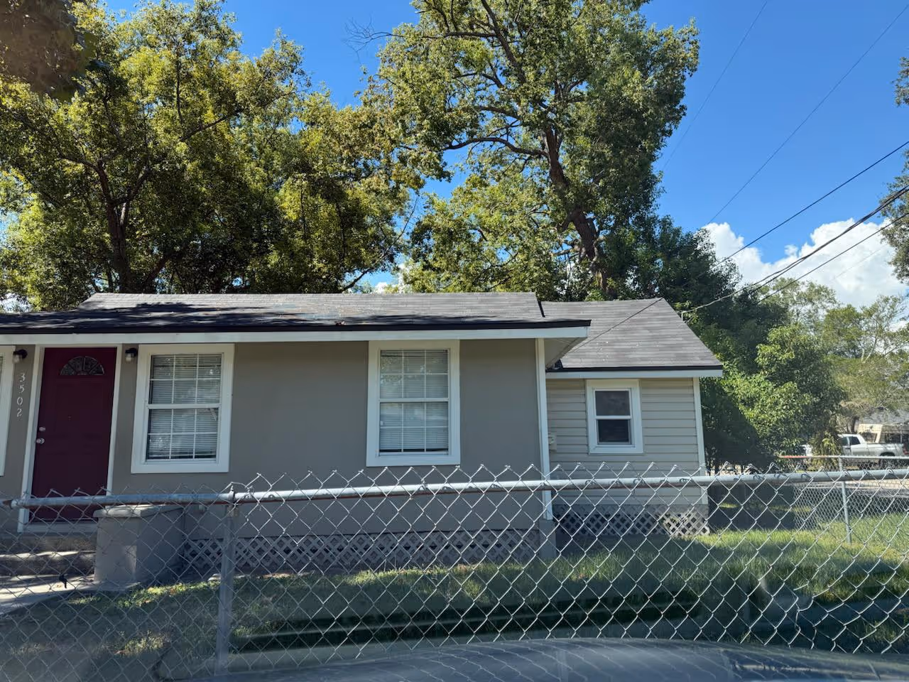 Single-story house with white exterior and black trim, a small front porch with stairs, landscaped front yard with grass and colorful plants.