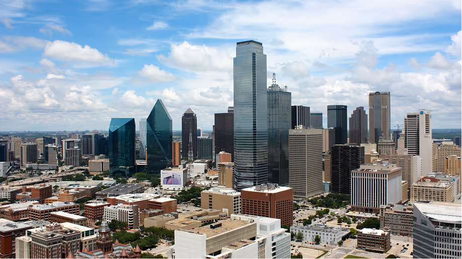 Cityscape of a downtown area with modern skyscrapers under a partly cloudy sky.